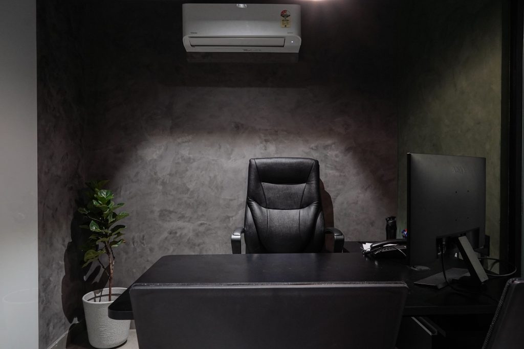 Minimalist office interior featuring leather chair, desk, monitor, plant, and air conditioner.
