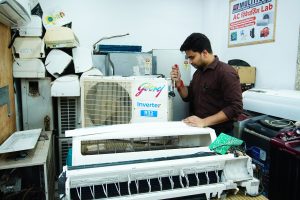 Technician repairing an air conditioner unit in New Delhi workshop.